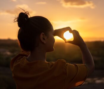 woman with her hands joining to form a heart during the sunset time